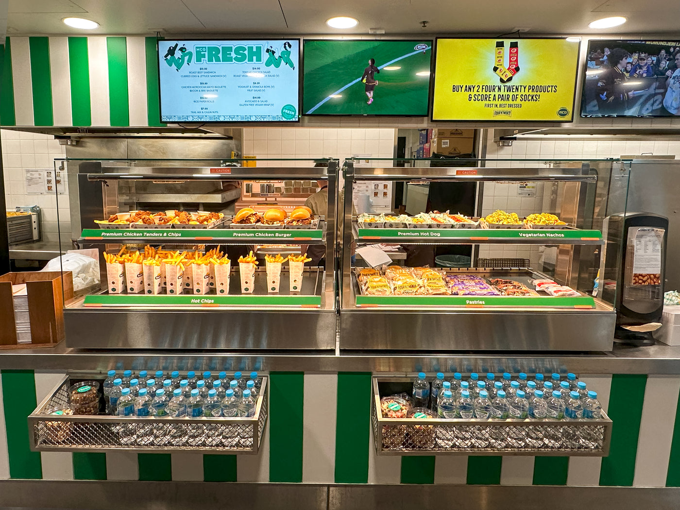 Fast food counter with various food items and screens displaying advertisements.