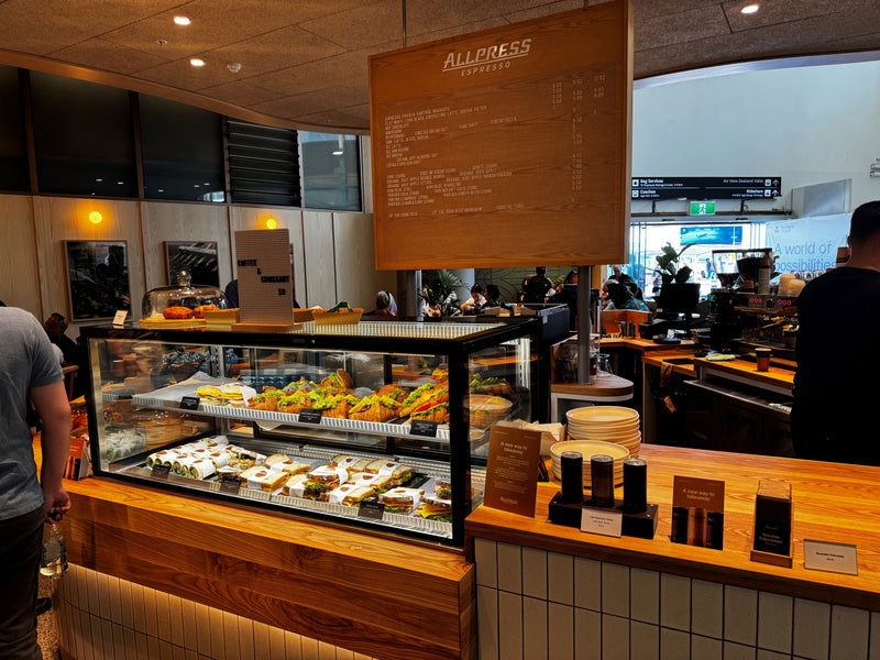 Coffee shop interior with a display case of food and 'Allpress' branding.
