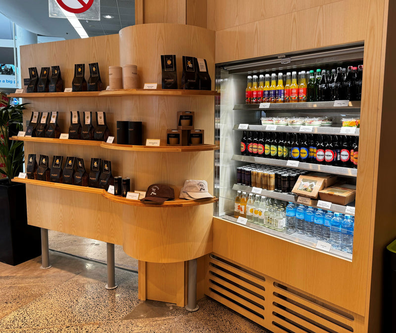 Wooden shelf with coffee products and a refrigerator with drinks in a store setting