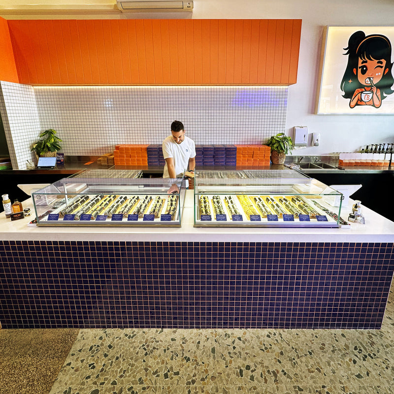 Person working behind a sushi bar with a colorful wall and artwork in the background