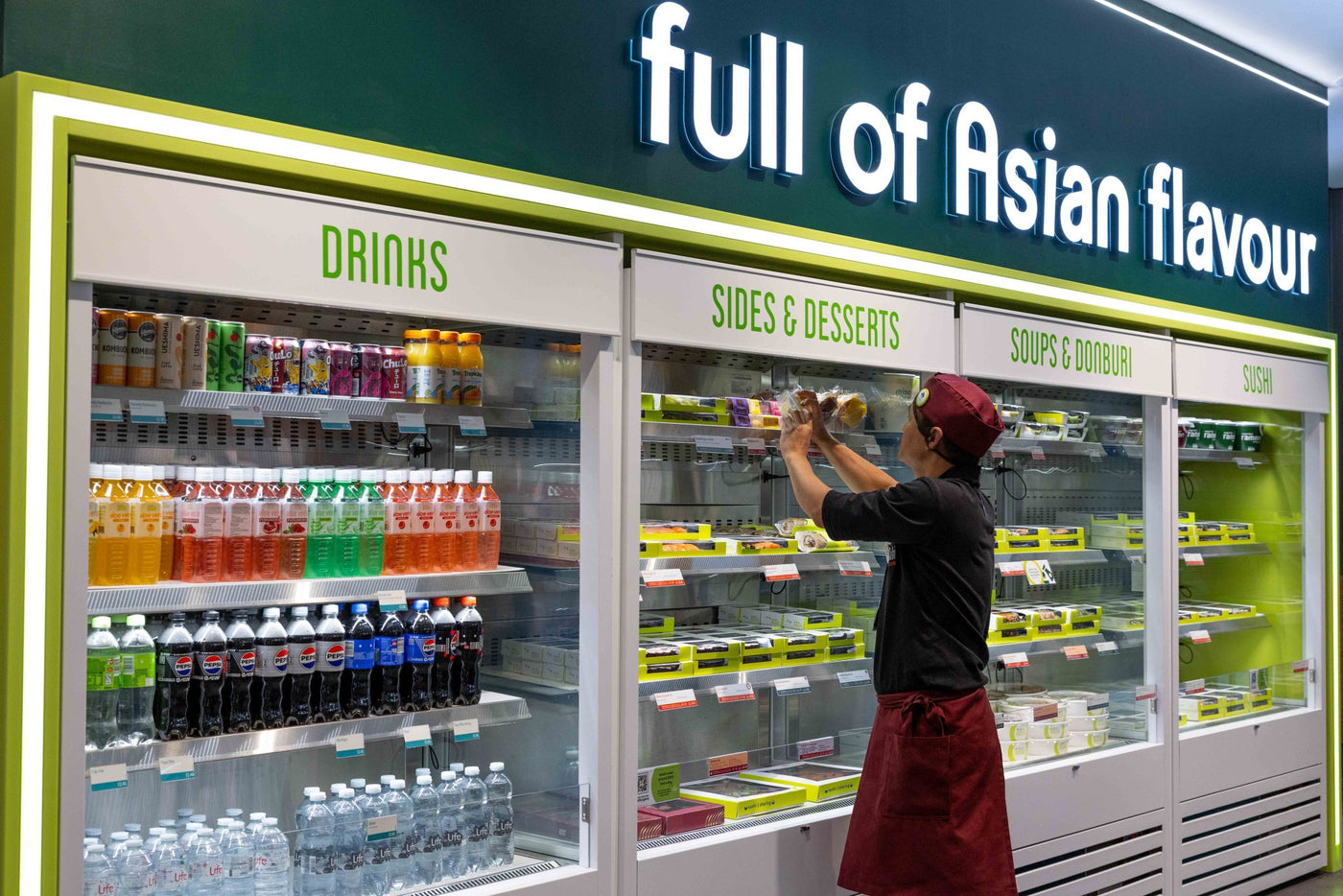 Person adjusting items inside a refrigerated display case labeled 'full of Asian flavour' in a store.